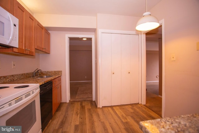 kitchen with light stone countertops, white appliances, sink, light hardwood / wood-style flooring, and hanging light fixtures