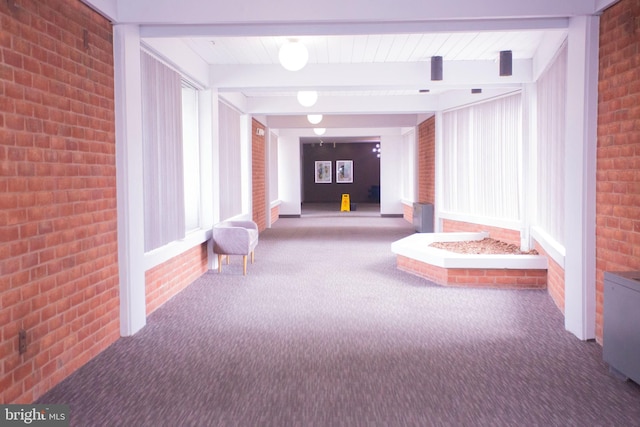 corridor with beamed ceiling, carpet flooring, and brick wall