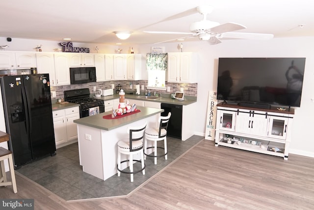 kitchen featuring a center island, black appliances, dark hardwood / wood-style floors, white cabinetry, and a breakfast bar area