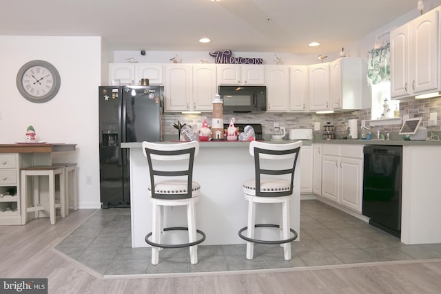 kitchen with black appliances, white cabinets, light wood-type flooring, and a breakfast bar area