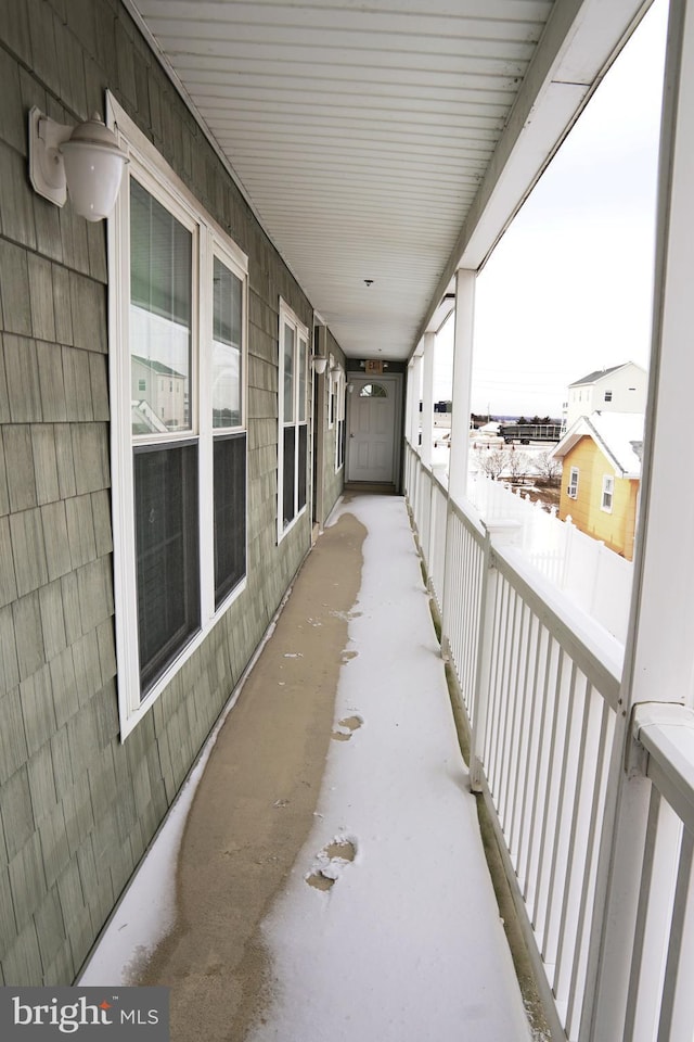 snow covered back of property featuring covered porch