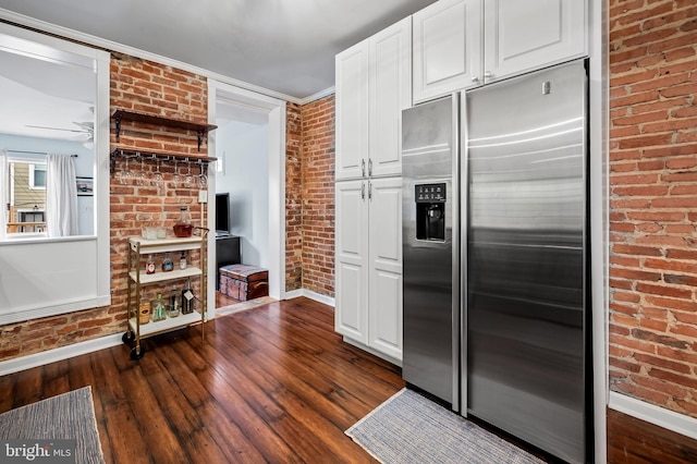 kitchen with white cabinets, ornamental molding, brick wall, and stainless steel refrigerator with ice dispenser