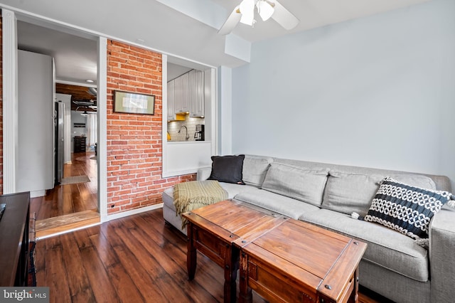 living room with sink, dark hardwood / wood-style floors, ceiling fan, and brick wall