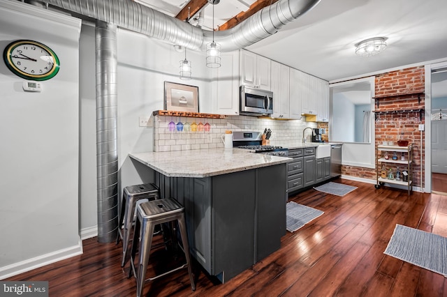 kitchen with gray cabinetry, hanging light fixtures, stainless steel appliances, white cabinets, and a kitchen bar