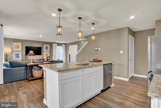 kitchen featuring stainless steel appliances, a kitchen island with sink, sink, pendant lighting, and white cabinets