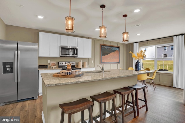 kitchen featuring white cabinetry, light stone countertops, hanging light fixtures, stainless steel appliances, and a center island with sink