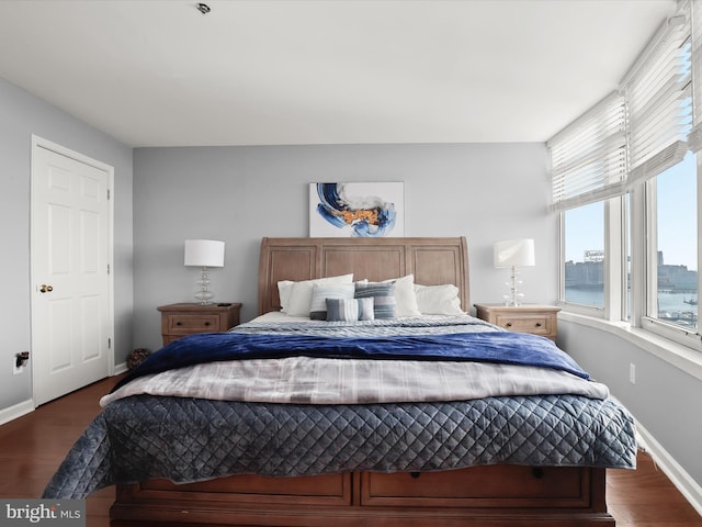 bedroom with dark hardwood / wood-style flooring and a water view