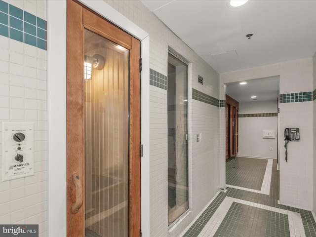 hall featuring dark tile patterned flooring and tile walls