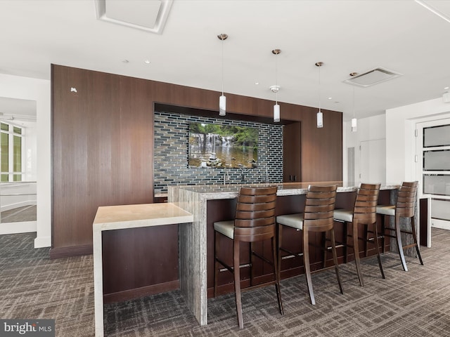 bar with pendant lighting, dark brown cabinets, wooden walls, and dark colored carpet