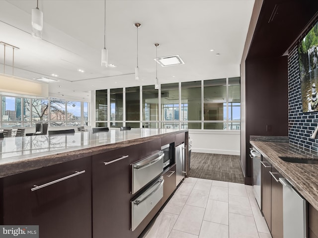 kitchen with backsplash, decorative light fixtures, sink, and stone counters