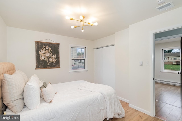 bedroom with a closet, hardwood / wood-style floors, a baseboard heating unit, and a notable chandelier