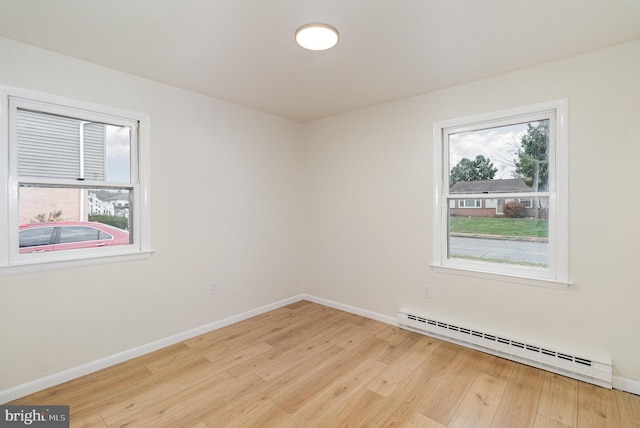 spare room featuring baseboard heating, a healthy amount of sunlight, and light wood-type flooring