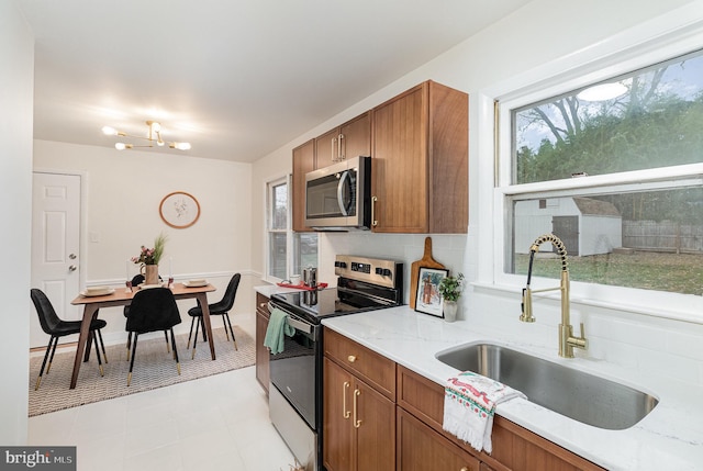 kitchen featuring light stone countertops, decorative backsplash, stainless steel appliances, sink, and a notable chandelier