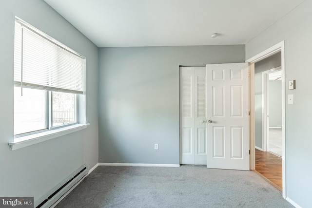 unfurnished bedroom with light colored carpet, a closet, and a baseboard heating unit