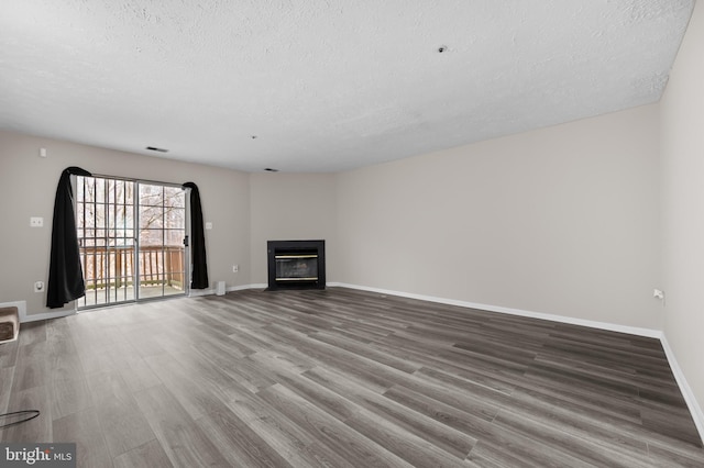 unfurnished living room featuring visible vents, a glass covered fireplace, a textured ceiling, wood finished floors, and baseboards