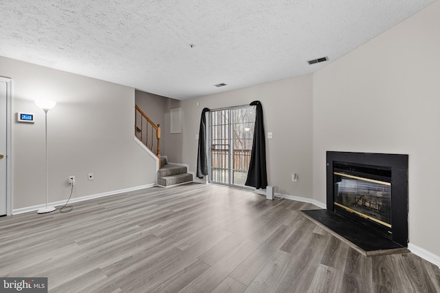 unfurnished living room featuring baseboards, visible vents, a glass covered fireplace, stairway, and wood finished floors