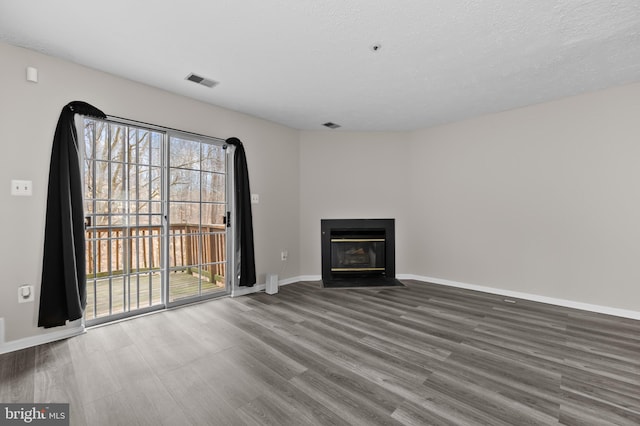 unfurnished living room with a fireplace with flush hearth, a textured ceiling, baseboards, and wood finished floors