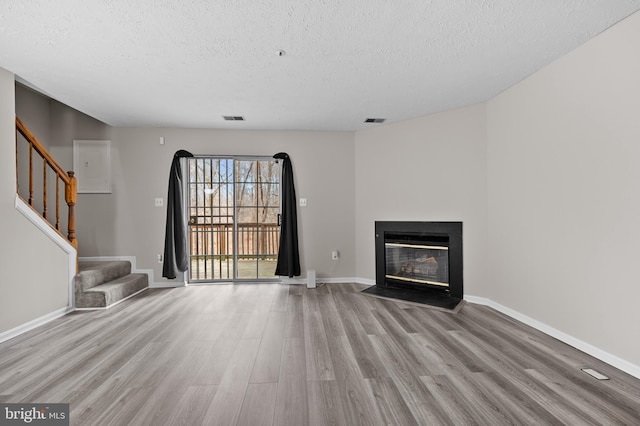 unfurnished living room featuring stairs, wood finished floors, a fireplace with flush hearth, and visible vents