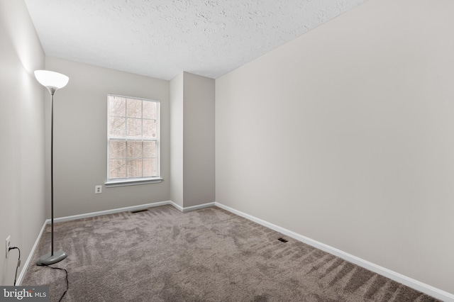 empty room with a textured ceiling, carpet, visible vents, and baseboards