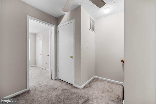 corridor with carpet, a textured ceiling, visible vents, and baseboards