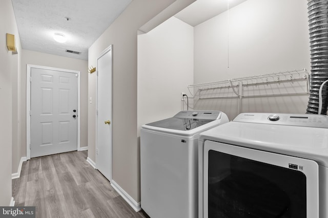 laundry room featuring a textured ceiling, laundry area, wood finished floors, baseboards, and washer and dryer