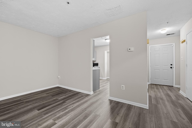 spare room with visible vents, a textured ceiling, baseboards, and wood finished floors