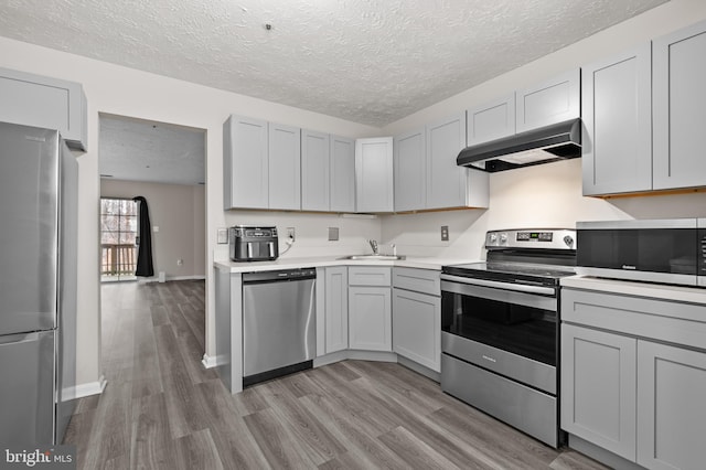 kitchen featuring under cabinet range hood, stainless steel appliances, light countertops, and light wood finished floors