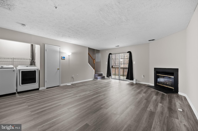 unfurnished living room featuring washing machine and clothes dryer, visible vents, stairway, a glass covered fireplace, and wood finished floors