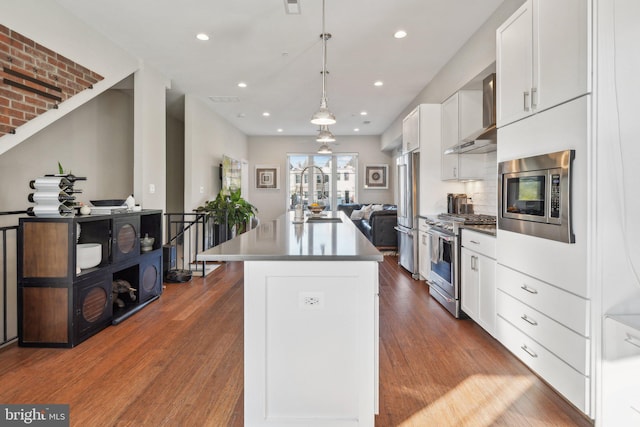 kitchen with pendant lighting, premium appliances, white cabinets, a kitchen island, and hardwood / wood-style flooring