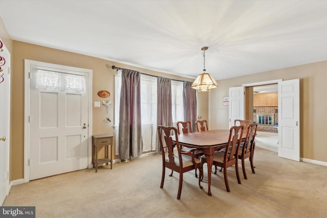 dining space featuring a brick fireplace, a healthy amount of sunlight, light colored carpet, and a notable chandelier