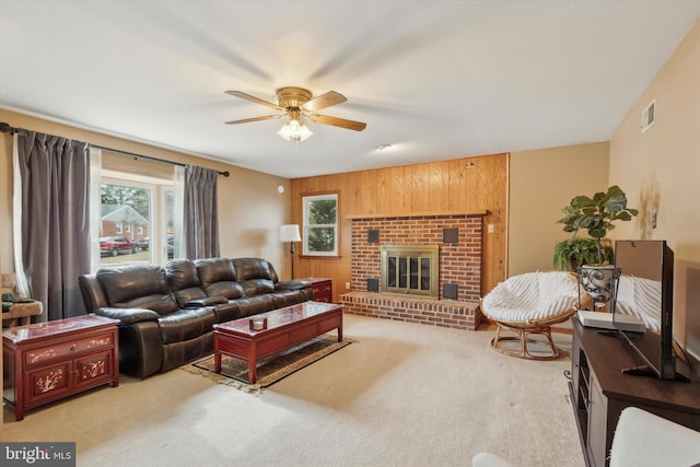 living room with ceiling fan, carpet flooring, a fireplace, and wood walls