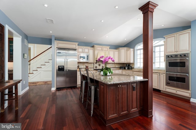 kitchen featuring decorative columns, decorative backsplash, light stone counters, built in appliances, and cream cabinets