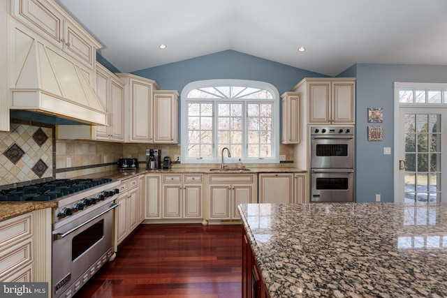 kitchen with cream cabinets, custom range hood, stainless steel appliances, and a sink