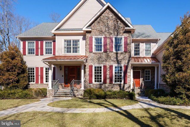 view of front facade with stone siding, a standing seam roof, metal roof, and a front lawn