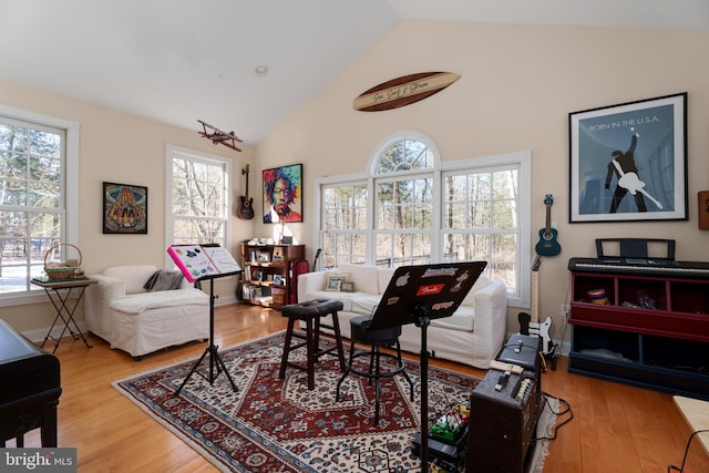 living area with a healthy amount of sunlight, baseboards, high vaulted ceiling, and wood finished floors