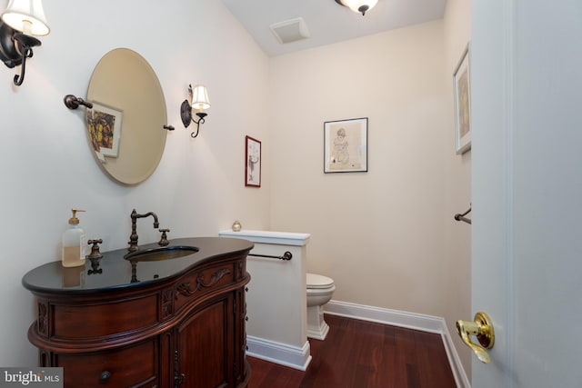 half bath with toilet, wood finished floors, vanity, and baseboards