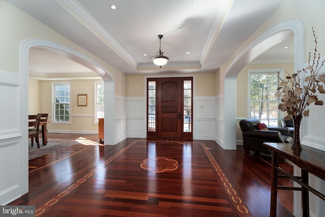 entryway with a tray ceiling, a wainscoted wall, and arched walkways