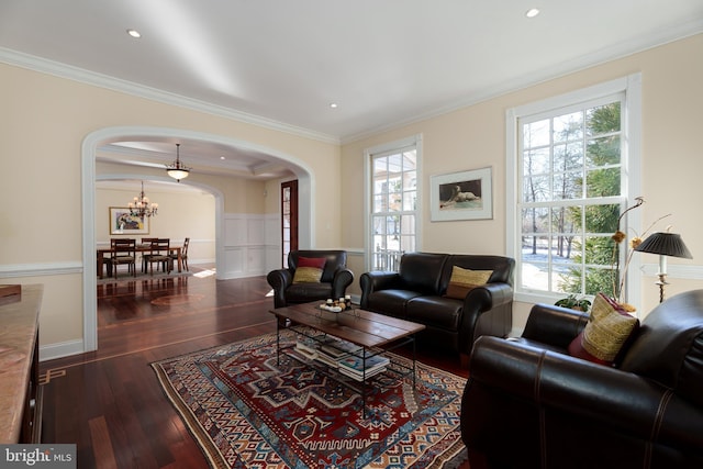 living room with arched walkways, ornamental molding, dark wood-type flooring, and a wainscoted wall