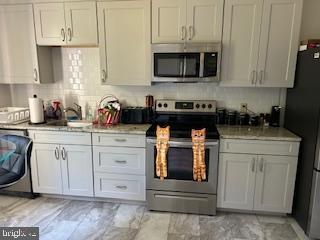 kitchen with white cabinets, stainless steel appliances, light stone countertops, and tasteful backsplash