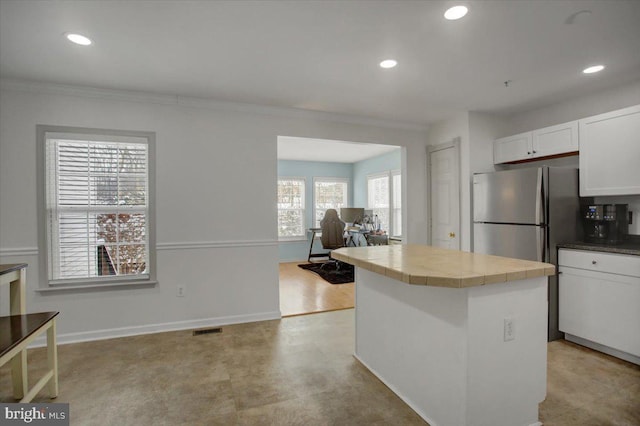 kitchen with white cabinets, tile counters, a kitchen island, stainless steel refrigerator, and crown molding