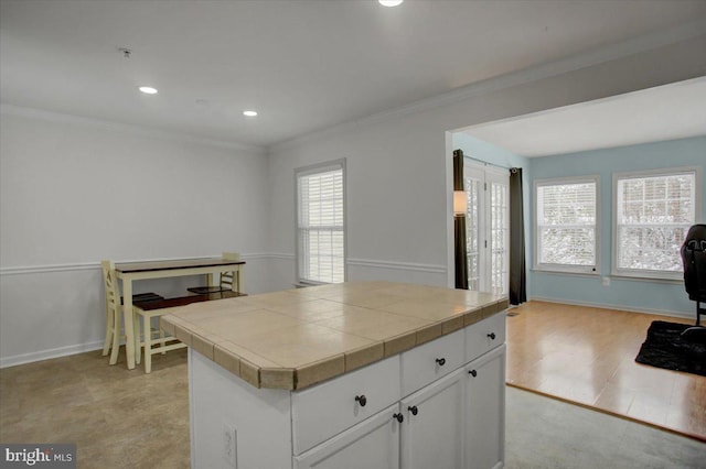 kitchen with light hardwood / wood-style floors, tile counters, white cabinets, a kitchen island, and ornamental molding