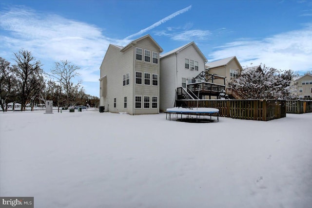 snow covered rear of property featuring a deck and a trampoline