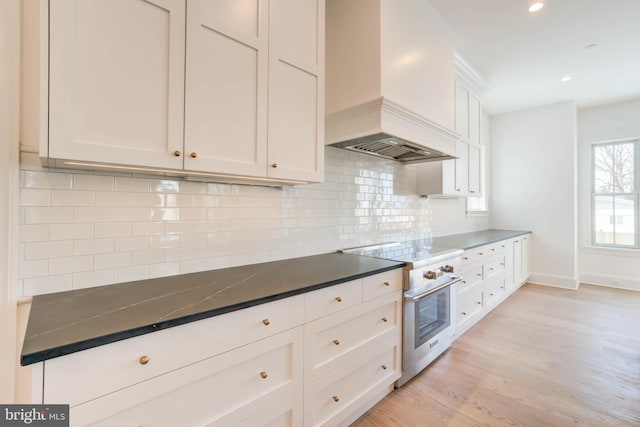 kitchen featuring custom exhaust hood, white cabinets, high end stainless steel range oven, decorative backsplash, and light wood-type flooring