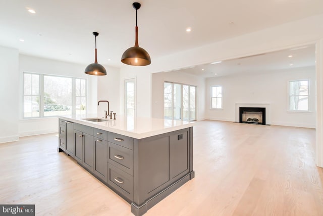 kitchen featuring gray cabinetry, a kitchen island with sink, sink, hanging light fixtures, and plenty of natural light