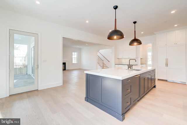 kitchen featuring white cabinetry, sink, pendant lighting, a kitchen island with sink, and light wood-type flooring