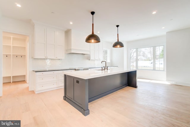 kitchen featuring custom range hood, sink, pendant lighting, white cabinets, and an island with sink