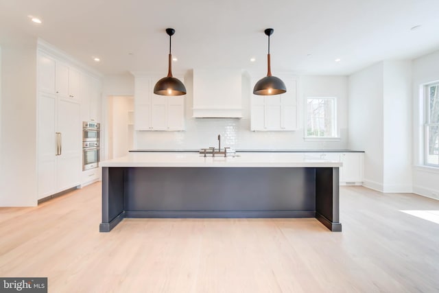 kitchen featuring decorative backsplash, light wood-type flooring, a spacious island, white cabinetry, and hanging light fixtures