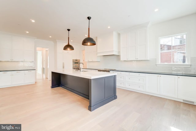 kitchen featuring sink, hanging light fixtures, a kitchen island with sink, white cabinets, and custom range hood