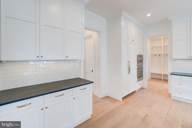 kitchen featuring light wood-type flooring, tasteful backsplash, dark stone counters, double oven, and white cabinetry