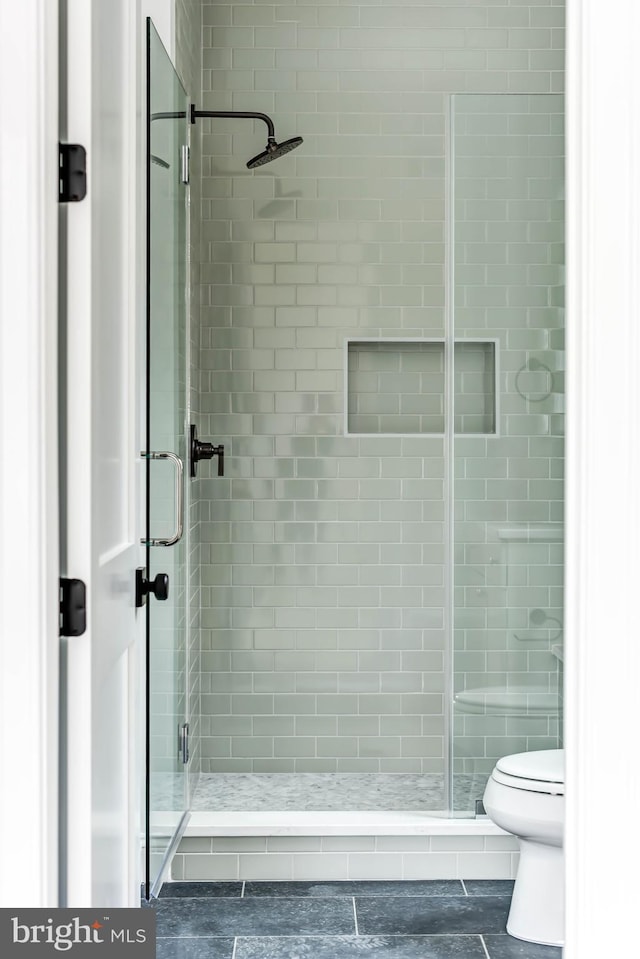 bathroom featuring a shower with door and toilet